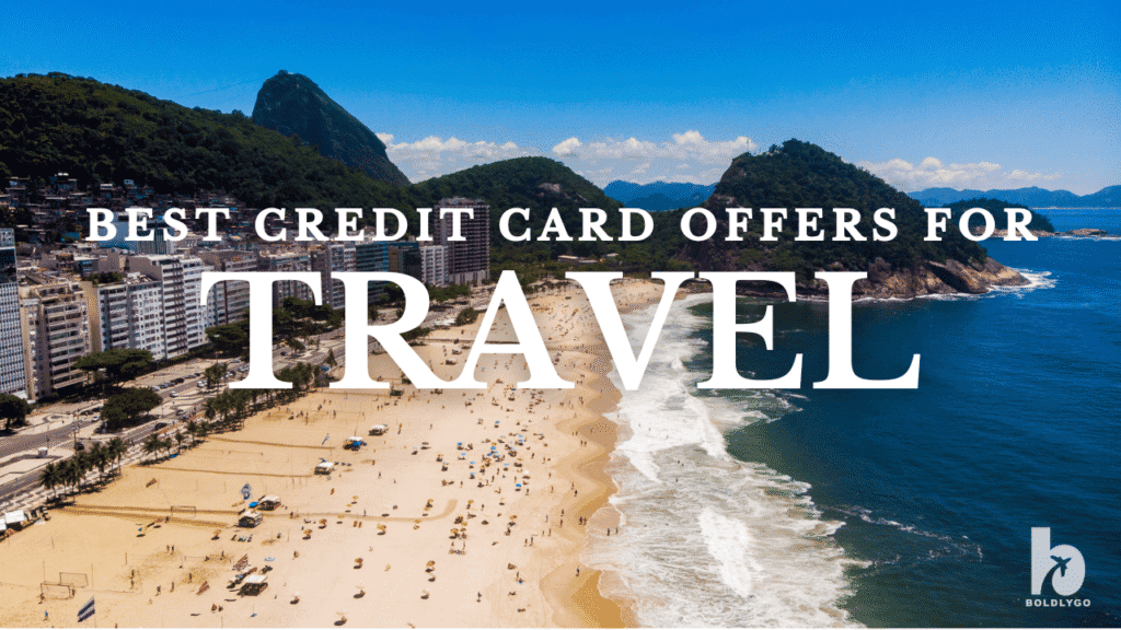 Aerial view of a sunny beach with people and waves along a coastline, with a city and green mountains in the background. Bold white text reads 'Best Credit Card Offers for Travel' with the Boldly Go logo in the bottom right corner