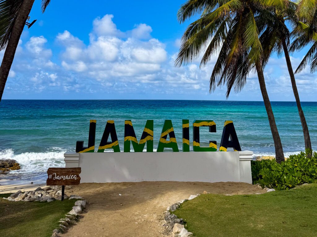 Colorful Jamaica sign overlooking the Caribbean Sea at Hyatt Zilara Rose Hall, framed by palm trees and ocean waves in Montego Bay.