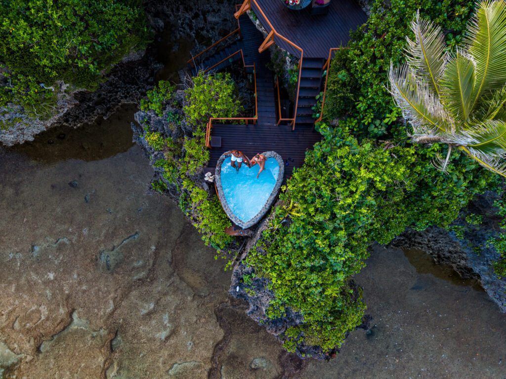 Overhead drone view of a couple relaxing in a heart-shaped cliffside plunge pool at Namale Resort & Spa in Fiji.