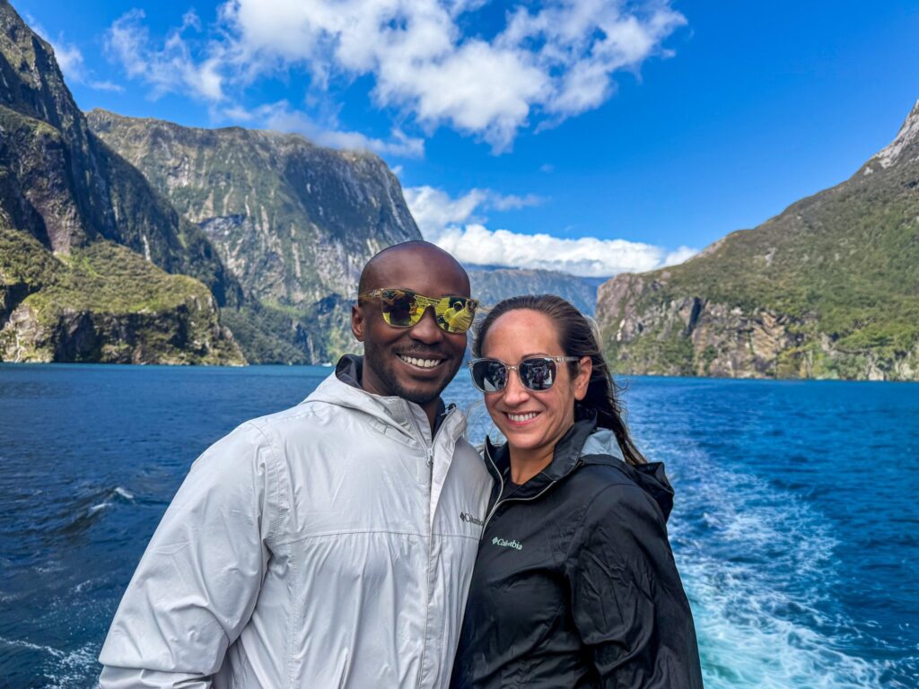 Couple smiling on Milford Sound cruise boat with mountains and fjord behind them