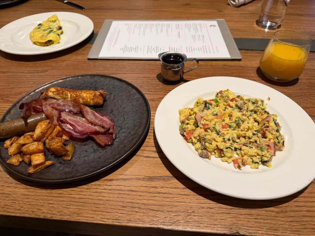 Breakfast buffet plate at Grand Hyatt Vail with scrambled eggs, bacon, sausage, potatoes, and orange juice