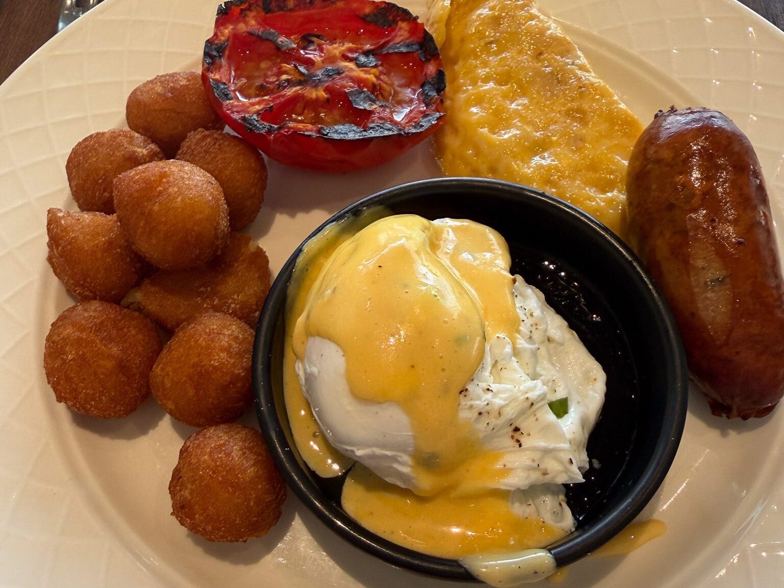 Breakfast plate at Hyatt Regency Malta with poached eggs, sausage, potato croquettes, grilled tomato, and polenta
