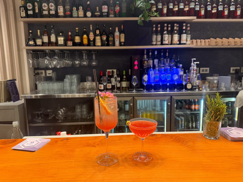 Two orange cocktails on a wooden bar counter with bottles displayed behind them