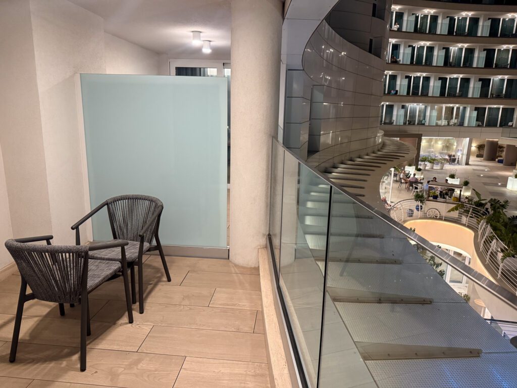 Suite balcony with two chairs and a glass railing overlooking the hotel piazza