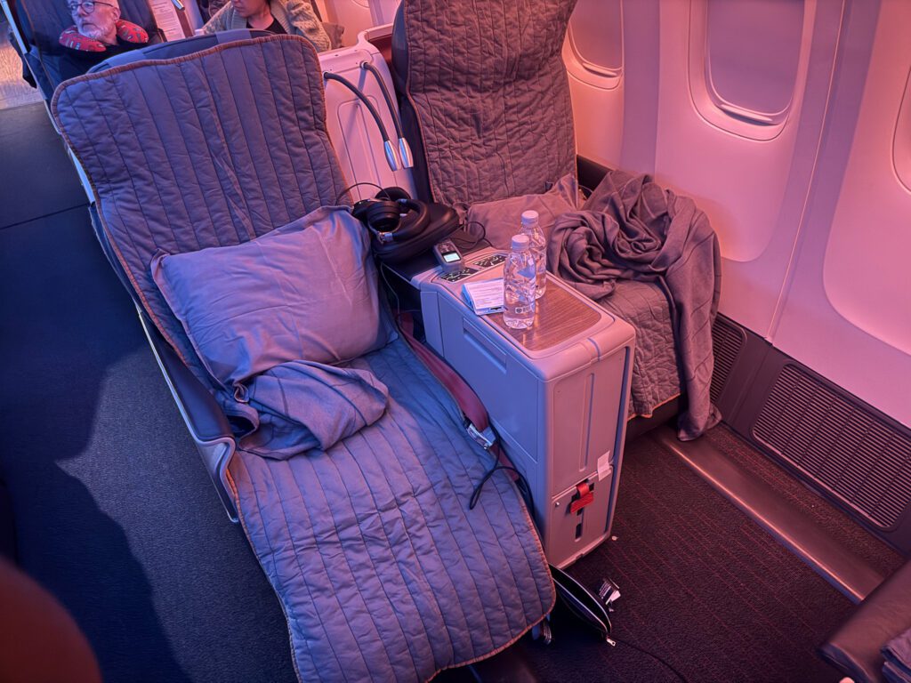 Paired business-class seats fitted with padded covers, pillows and blankets under pink cabin lighting.