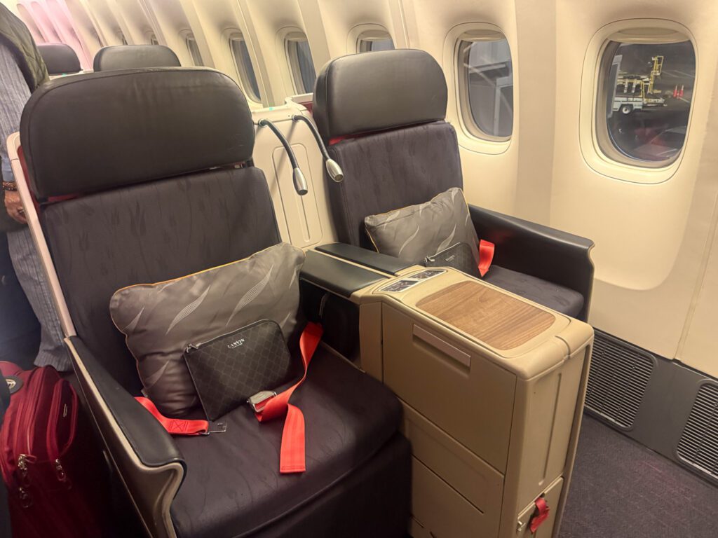 Paired Turkish Airlines 777 business-class window seats with pillows, red seat belts and amenity kits.