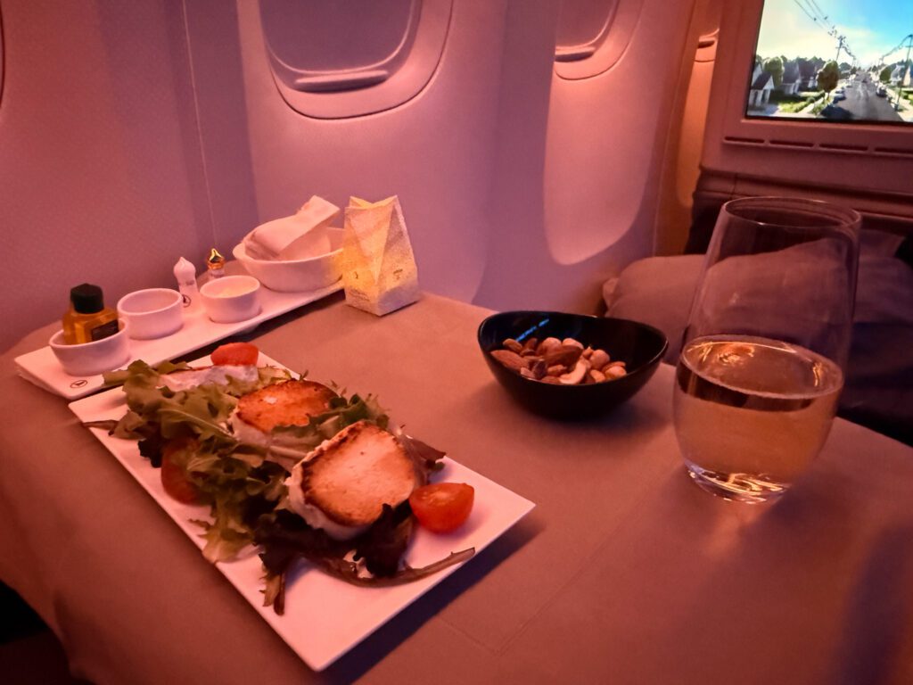 Grilled goat cheese salad served with mixed nuts and a drink on a business-class tray table.